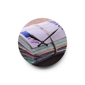 May include: Round wall clock featuring a stack of Euro banknotes secured with twine. The clock face displays the currency, with black clock hands indicating the time. The background is a wooden surface.