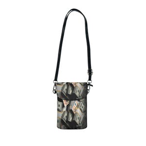 May include: A black crossbody bag with a strap and a flap closure. The bag's front features a print of stacks of US dollar bills. The strap is black and adjustable. The bag is designed to be worn over the shoulder.