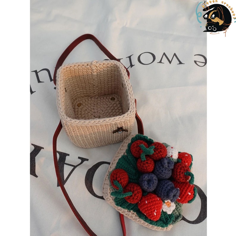 May include: A crocheted strawberry and blueberry tote bag with a beige crocheted box. The tote bag has a red strap and is open to reveal the crocheted fruit inside.