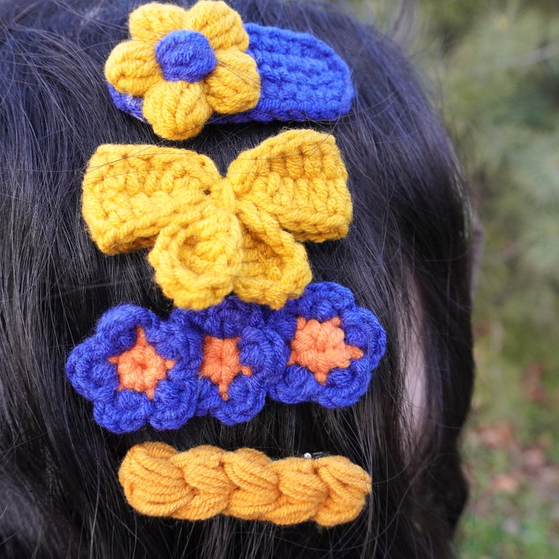 May include: A set of five crocheted hair clips in yellow and blue. The clips are in the shape of flowers and bows.