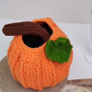 May include: Orange crocheted pumpkin with a brown crocheted handle and a green crocheted leaf.