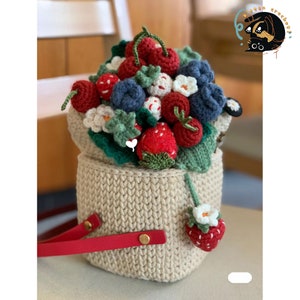 May include: A crocheted basket filled with a bouquet of red and white strawberries, blue blueberries, and green leaves. The basket has a red handle and is made of beige yarn.