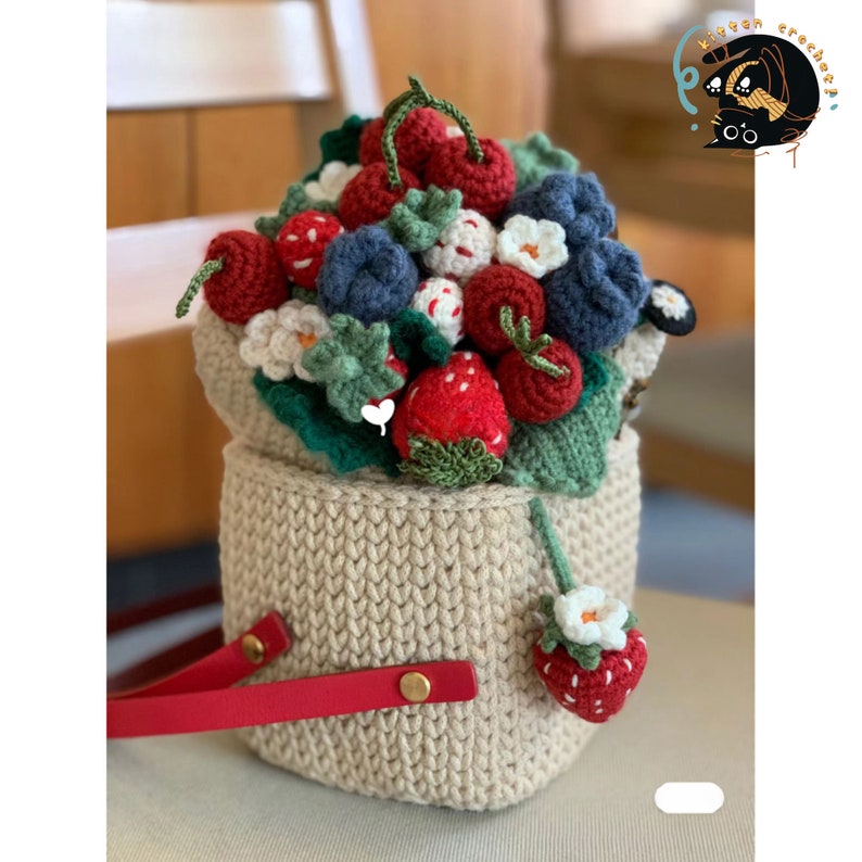 May include: A crocheted basket filled with a bouquet of red and white strawberries, blue blueberries, and green leaves. The basket has a red handle and is made of beige yarn.