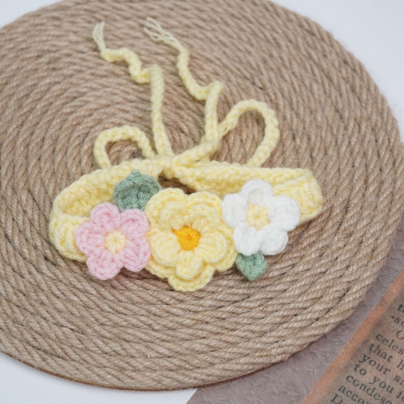 May include: A yellow crocheted headband with three crocheted flowers. The flowers are yellow, pink, and white. The headband has a tie closure.