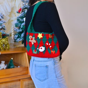 May include: A red and green crocheted Christmas tree-shaped bag with a gingerbread man, a star, a candy cane, a Santa Claus, and a gift box. The bag is worn over the shoulder of a person wearing a black shirt and blue jeans.