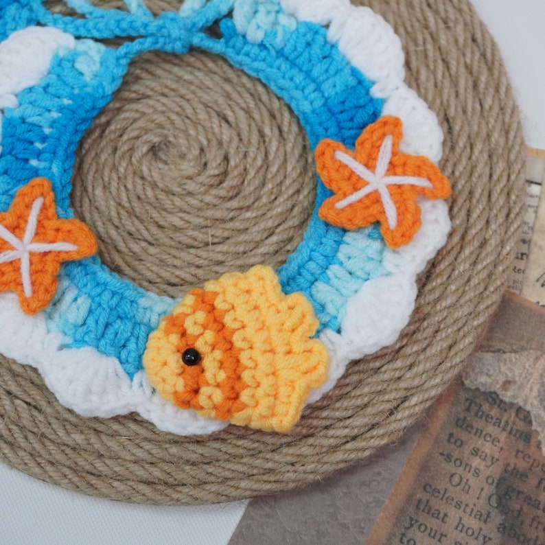 May include: A crocheted wreath with a blue and white wave design, featuring a yellow and orange fish and two orange starfish.
