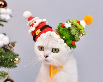 May include: A white cat wearing a crocheted Christmas hat with a Santa Claus and a Christmas tree design. The hat is red, green, and white.