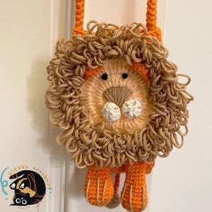 May include: A crocheted lion-shaped purse with a brown mane, orange body, and orange strap. The purse has a white nose and black eyes.