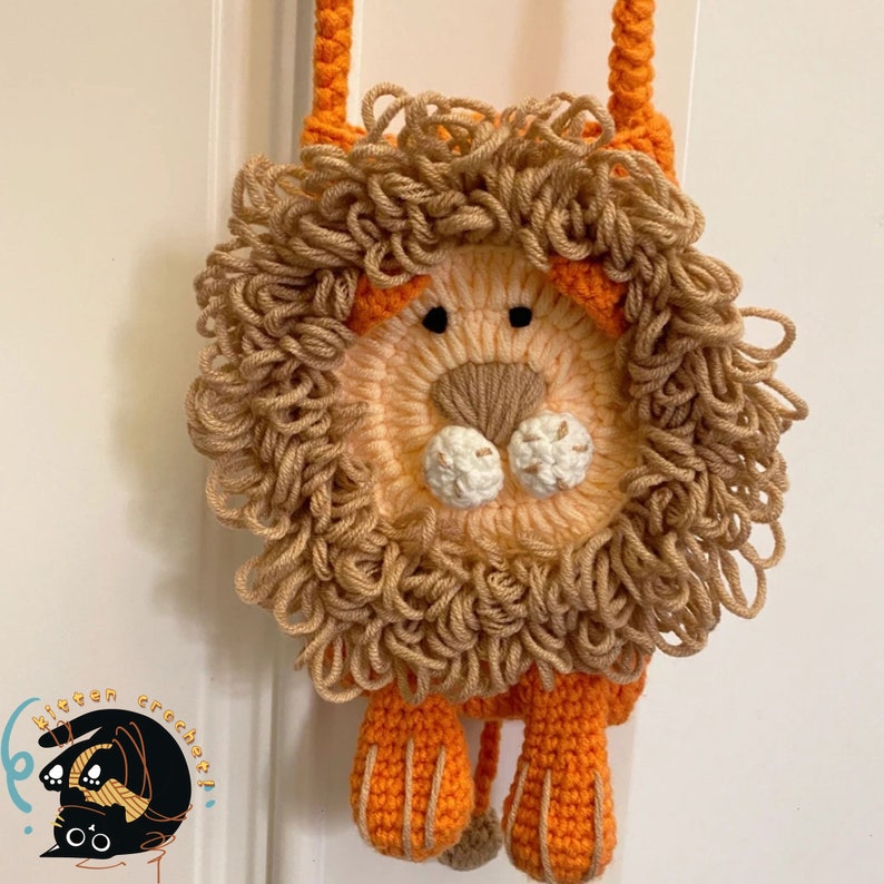 May include: A crocheted lion-shaped purse with a brown mane, orange body, and orange strap. The purse has a white nose and black eyes.