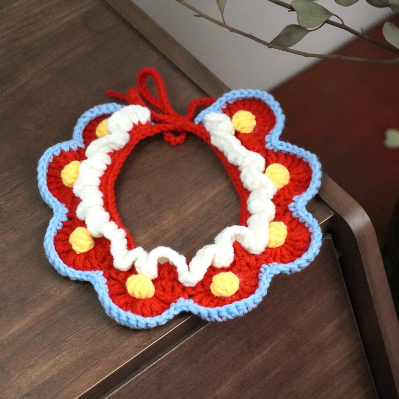 May include: A red, white, and blue crocheted collar with yellow polka dots. The collar is made of yarn and has a scalloped edge.