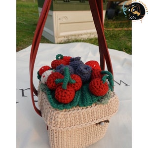 May include: A crocheted basket with a red and green handle, filled with crocheted strawberries and blueberries. The basket is beige and has a woven texture.