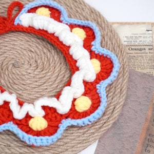 May include: A red, white, and blue crocheted wreath with yellow polka dots. The wreath is made of yarn and has a scalloped edge.