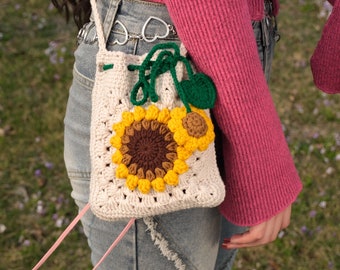 May include: A white crocheted bag with a sunflower design. The bag has a pink strap and is worn over the shoulder.