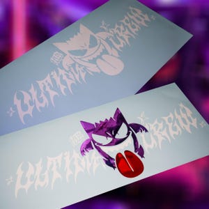 Peut inclure: Deux autocollants en vinyle rectangulaires représentant un personnage Gengar violet stylisé avec une langue rouge, accompagnés du texte "ULTIMA CREW" dans une police gothique pointue. Les autocollants sont sur un papier support bleu clair.