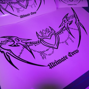 Op de afbeelding: Zwart-wit grafisch ontwerp met een hart met vleugels en kettingen. De tekst "Ultimate Crew" is geschreven in een gotisch lettertype.