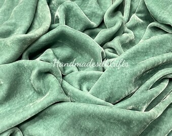 May include: A close-up shot of a luxurious, sage green velvet fabric. The fabric is draped and folded, creating soft shadows and highlights. The text "HandmadesilkGifts" is visible on the fabric.