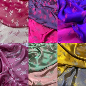 Puede incluir: Una colección de muestras de tela de satén en varios colores, incluyendo rosa, morado, azul, magenta, verde, dorado y gris. Cada pieza de tela presenta un patrón floral repetitivo en un tono más claro y brillante sobre la superficie lisa.