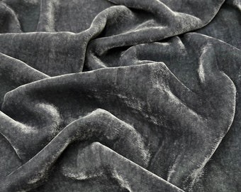 May include: Close-up of a dark gray velvet fabric with a soft, textured surface. The fabric is draped and folded, creating a luxurious and elegant look.