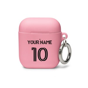 May include: Pink silicone case for wireless earbuds with a silver carabiner clip. The case has the text "YOUR NAME" and the number "10" printed on it.