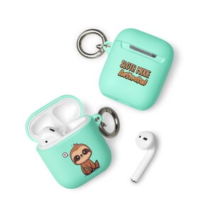 May include: A mint green Airpods case with a sloth design and the text "Sloth Mode Activated". The case has a keychain attached. The case is open and shows a white Airpod inside.