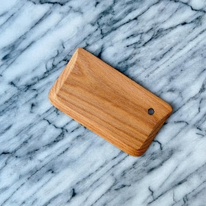 Può includere: Un tagliere rettangolare in legno con angoli arrotondati e un piccolo foro. Il tagliere è realizzato in legno marrone chiaro e presenta un motivo a venature naturali. Il tagliere misura circa 20 cm di lunghezza e 13 cm di larghezza.