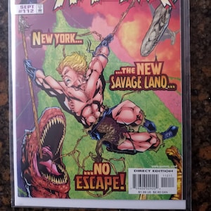 Puede incluir: Portada de cómic con el personaje Kazar, con el texto "What If... Starring Kazar." La ilustración muestra a Kazar balanceándose por una jungla, con un dinosaurio y el texto "The New Savage Land." El cómic está etiquetado como "Direct Edition."
