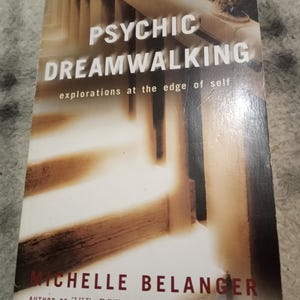 May include: A book cover for "PSYCHIC DREAMWALKING" with the tagline "explorations at the edge of self." The cover has a blurred image of a staircase and columns. The author's name, MICHELLE BELANGER, is printed in red at the bottom.