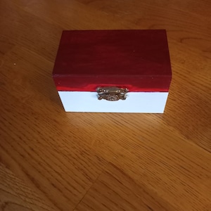 May include: A small wooden box with a red top and a white bottom. The box has a brass latch.