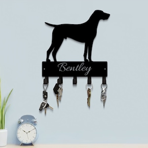 May include: Black metal key holder with a silhouette of a dog and the name "Bentley" engraved on the top. Five hooks are attached to the bottom of the holder.