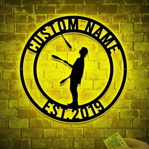 May include: Black metal wall clock with a silhouette of a person juggling. The clock face reads "CUSTOM NAME EST 2019".