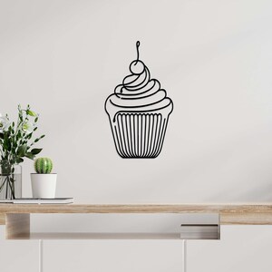 May include: Black metal cupcake wall art. The cupcake features a swirl of frosting, a cherry on top, and a detailed paper liner. This decorative piece is designed to be mounted on a wall and adds a touch of whimsy to any space.