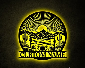 May include: A black metal wall art piece with a desert landscape design. The art features a sun, mountains, cacti, and stars. The words "CUSTOM NAME" are displayed below the design.