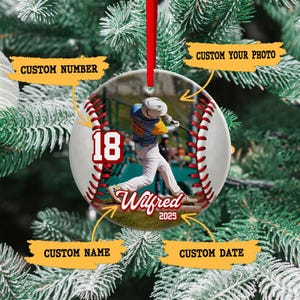 May include: A baseball-themed Christmas ornament with a red ribbon for hanging. The ornament features a baseball design with red stitching and a photo of a baseball player. The number "18", the name "Wilfred", and the year "2025" are also displayed.
