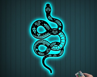 May include: A black snake with floral details is illuminated in a turquoise glow against a dark blue woodgrain background. A remote control with color changing buttons is visible in the lower right corner.