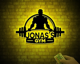 May include: A yellow neon sign with a silhouette of a person lifting weights. The sign says "Jonas's Gym" in black text.