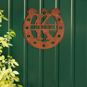 May include: A rusty brown metal horseshoe with the letter K in the center and the name Kelly written inside the horseshoe.