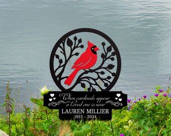 May include: A black metal garden stake with a red cardinal silhouette perched on a branch. The stake has a sign that reads "When cardinals appear a loved one is near" and "LAUREN MILLIER 1953 - 2024".