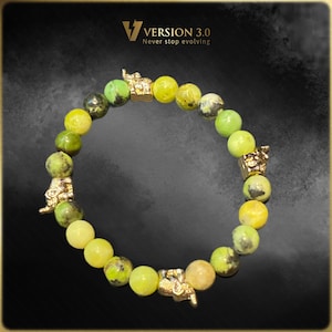 May include: A beaded bracelet featuring yellow and green stone beads with gold-colored decorative accents. The bracelet has the text "VERSION 3.0 Never stop evolving" in the upper left corner. The bracelet is on a black background.
