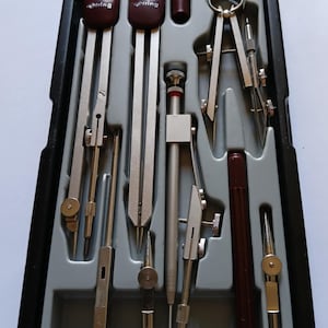 以下が含まれることがあります： 黒いケースに入った製図用具のセット。コンパス、ディバイダー、その他の描画ツールが含まれています。ツールはシルバーとブラウンで、ケースはグレーです。「rotring」のブランド名が一部のツールに表示されています。