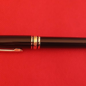 May include: A black and gold fountain pen with a clip on the side.