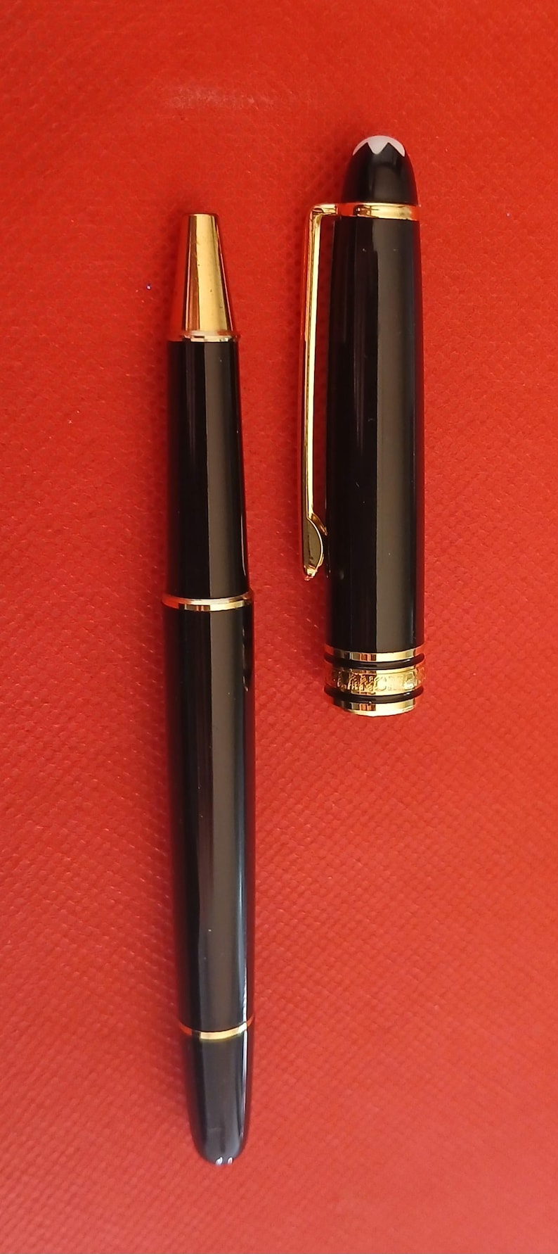 May include: Two black pens with gold accents. The pen on the left has a black cap and a gold band near the tip. The pen on the right has a white star on the cap and a gold band near the tip.