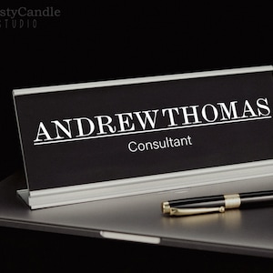May include: A black desk nameplate with silver trim. The nameplate reads "ANDREW THOMAS" and "Consultant".
