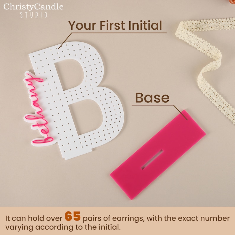 May include: White acrylic letter B with a pink base and a pink inscription that reads "bethany". The letter has a dotted surface and is designed to hold over 65 pairs of earrings.