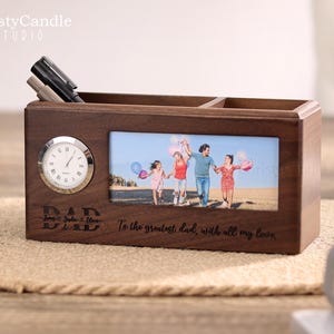 May include: A wooden desk organiser with a clock, a photo frame, and two compartments for pens or pencils. The photo frame shows a family of four walking on a beach. The organiser is engraved with the word "DAD" and the text "To the greatest dad, with all my love."