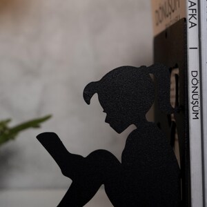 May include: Black metal bookends shaped like a girl sitting and reading a book. The bookends are holding up two books with the title "D&ouml;n&uuml;ş&uuml;m" by Franz Kafka.