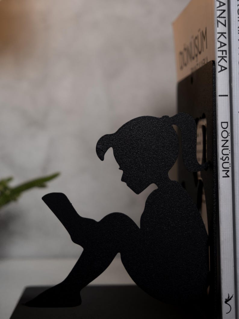 May include: Black metal bookends shaped like a girl sitting and reading a book. The bookends are holding up two books with the title "D&ouml;n&uuml;ş&uuml;m" by Franz Kafka.