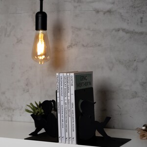 May include: Black metal bookends shaped like people reading. The bookends are holding up a stack of books with titles in German and English.