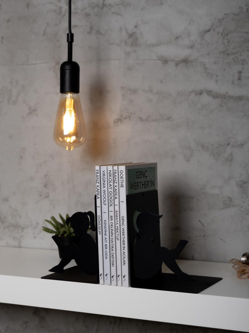 May include: Black metal bookends shaped like people reading. The bookends are holding up a stack of books with titles in German and English.