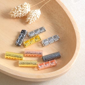 May include: Assortment of metal hair tie ends in various finishes, including gold, silver, and black. The ends are cylindrical and have a textured surface.