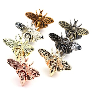 May include: A collection of decorative bee-shaped pins in various metallic finishes, including gold, silver, bronze, and rose gold. The pins feature detailed wing and body designs, perfect for adding a touch of nature-inspired flair to clothing or accessories.
